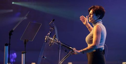 Penny Mallory giving a motivational speech in front of a podium.