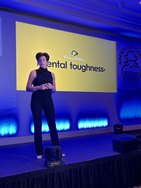 Image of motivational speaker Penny Mallory stood on stage with blue lighting with mental toughness on the screen